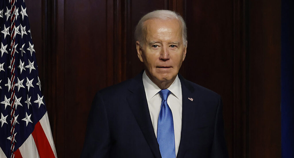 President Joe Biden in a black suit with an American flag pin and a blue tie.