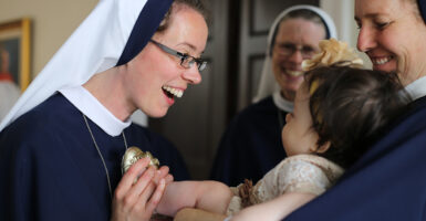 A nun smiles joyfully at a baby held by another nun.