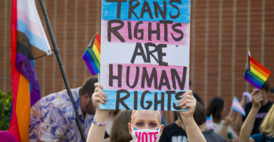 Woman holds sign reading "trans rights are human rights" while wearing a face mask reading "Vote"