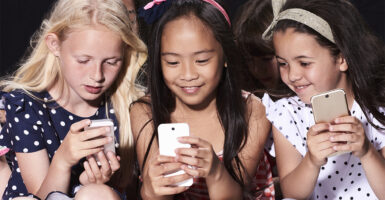 Three little girls sitting together looking at their smartphone screens