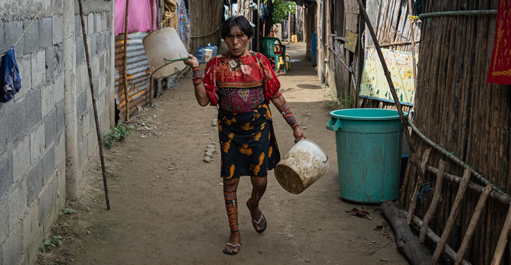 A woman wearing traditional indigenous clothes walks down an alley of shacks in Panama.