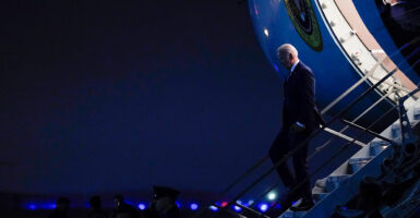 President Joe Biden walks down the steps of Air Force One in a suit at night.