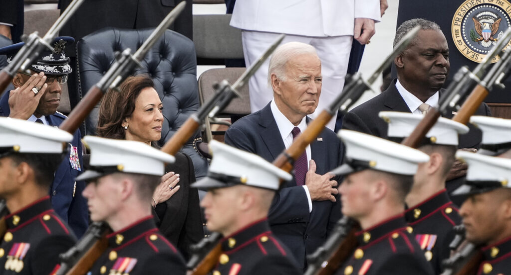 Kamala Harris, Joe Biden, and Lloyd Austin in suits stand behind members of the military in uniform