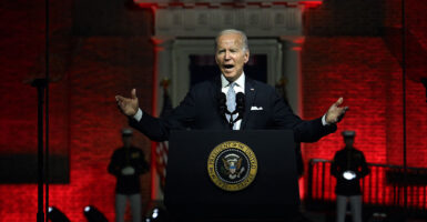 President Joe Biden gestures in a black suit in front of Philadelphia's Independence Hall behind the presidential seal