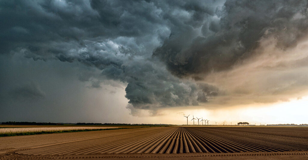 Storm clouds roll over a large farm field.
