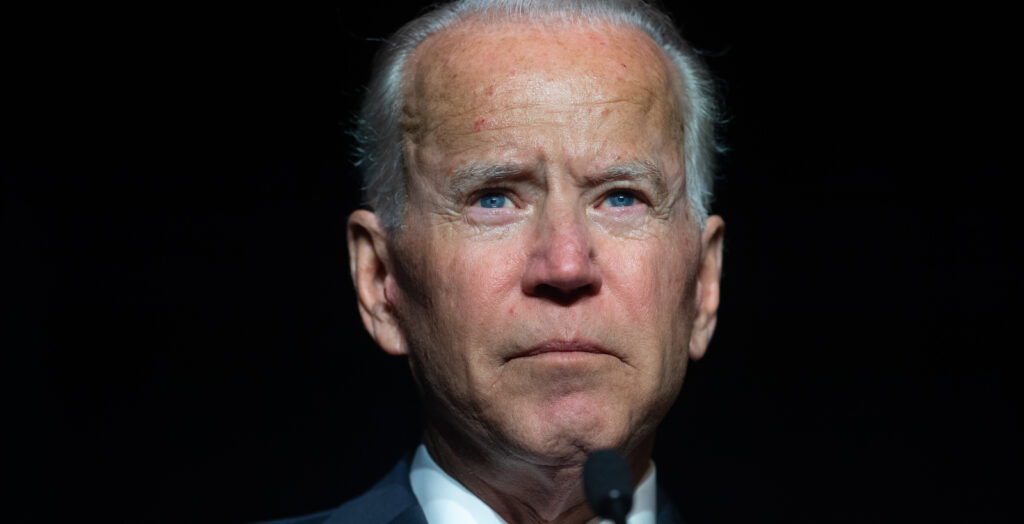 President Joe Biden grimaces while looking ahead in front of a black background