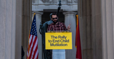 Conservative commentator Matt Walsh speaks in front of an American flag and behind a sign reading "The Rally to End Child Mutilation"
