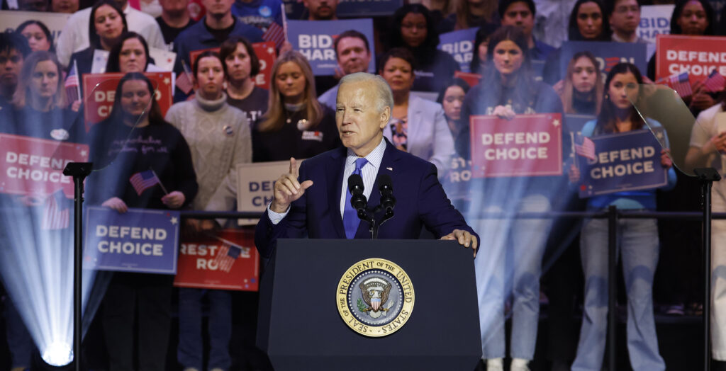 President Joe Biden speaks at a rally at a podium in a suit with a crowd behind him