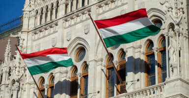 Hungarian flags fly on the Hungarian Parliament Building on a sunny day.