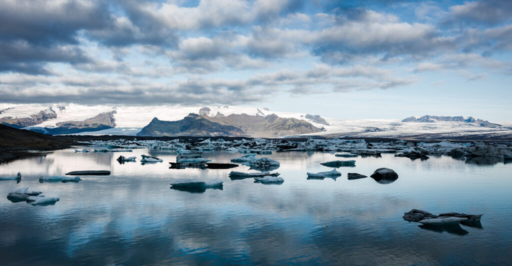 Icebergs drift in the ocean with snow capped mountains in the background.