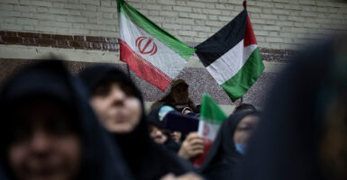 A man sits behind veiled women under an Iranian flag and a Palestinian flag.