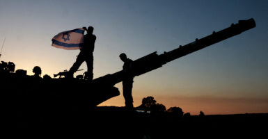 An Israeli soldier waves an Israeli flag on top of a tank as the sun sets.