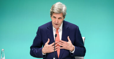 John Kerry in a blue suit gestures toward himself