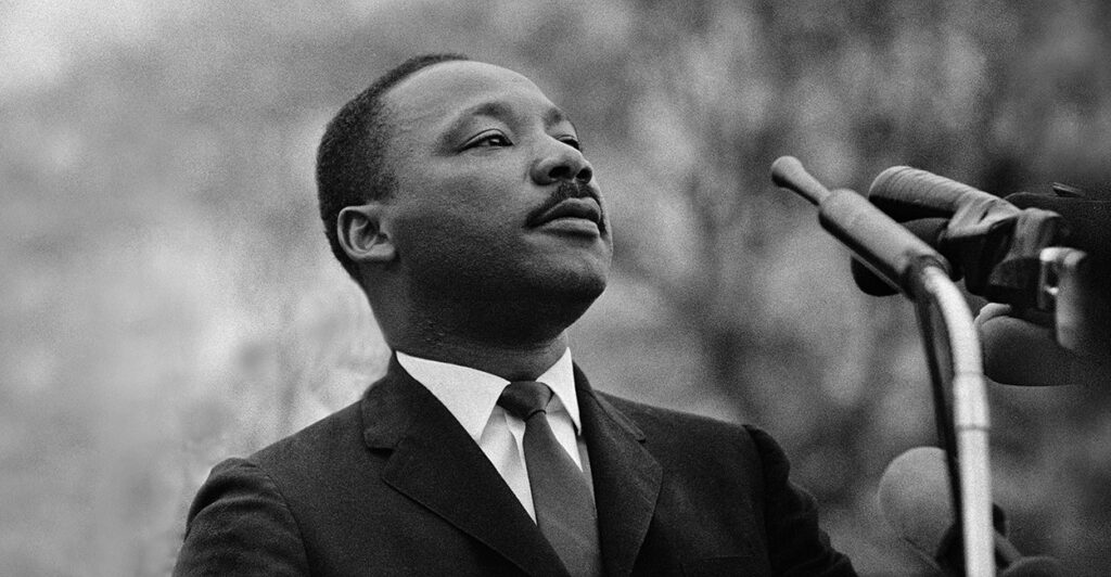 A black and white photo shows Martin Luther King Jr. speaking into a microphone.