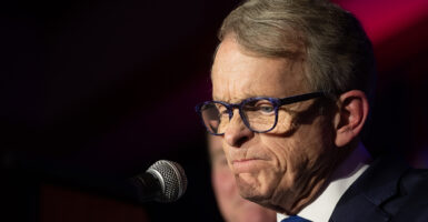 Ohio Governor Mike DeWine grimaces while wearing a suit in front of a microphone
