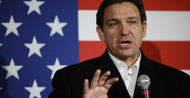 Ron DeSantis in a black suit stands in front of an American flag