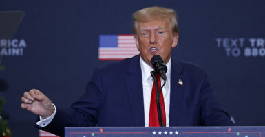 Donald Trump in a blue suit and red tie speaking at a microphone
