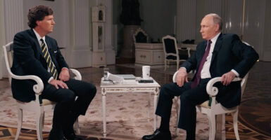 Tucker Carlson and Vladimir Putin, each in suits, sit across from one another.