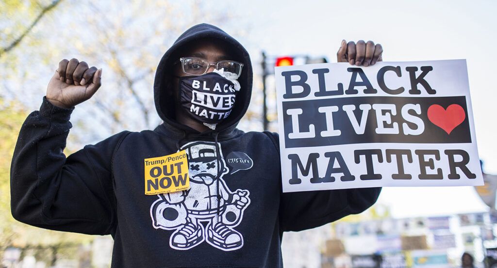 A female protester holds a sign reading "Black Lives Matter" as she also wears a face mask with "Black Lives Matter."