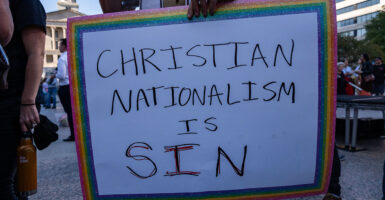 A sign with a rainbow frame reading "Christian Nationalism Is Sin."
