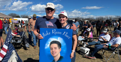 Lane and Martha O. Johnson stand together holding a large sign with their grandson's name and photo.