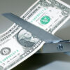 U.S. dollar bill is cut in half with scissors.