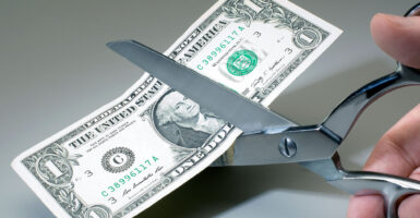 U.S. dollar bill is cut in half with scissors.