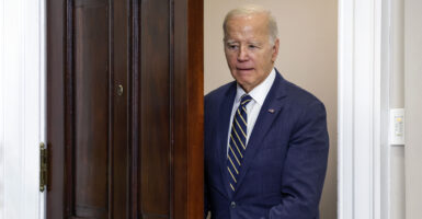 President Joe Biden opens a brown, wood door with a confused look on his face.