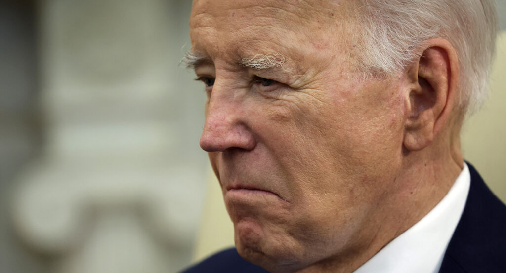 Joe Biden looks down with a grimace in a black suit