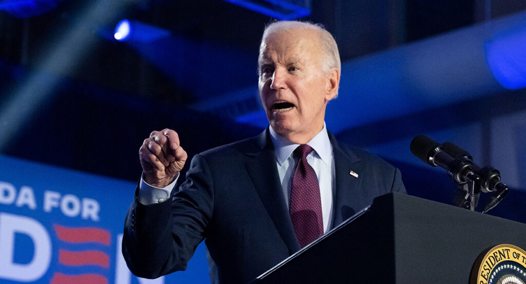 President Joe Biden angrily gestures in a blue suit with an American flag pin