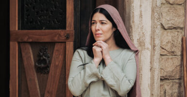 Elizabeth Tabish stands in traditional Biblical dress while portraying Mary Magdalene on the set of "The Chosen." She wears a long light blue tunic and a pale purple scarf on her head.