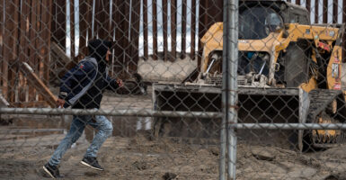 A man with a backpack and hoodie is seen running through an opening in the border wall.