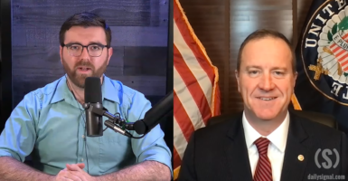 Split screen with Daily Signal reporter Tony Kinnett on a microphone on the left side interviewing Senator Eric Schmitt in a suit and tie on the right side