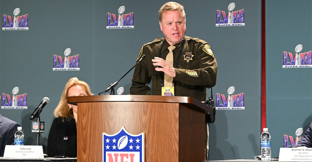 Sheriff McMahill stands at a podium with the NFL logo on it.. Behind him are panels with the Super Bowl LVIII logo on it.