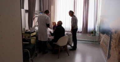 A doctor and family members stand around a hospital bed with a dying person.