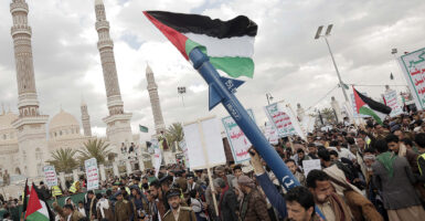 Houthi supporters protest in Yemen's capital, Sanaa, with one man holding a rocket and a Palestinian flag.