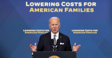 President Joe Biden delivers a speech behind a black podium Words behind him read "lowering costs for American families"