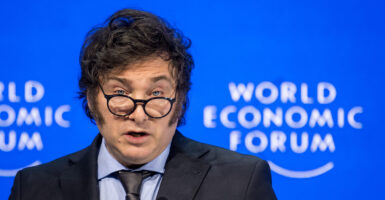 Argentina's president Javier Milei delivers a speech at the World Economic Forum, with spectacles lowered on his nose and a bright blue background behind him.