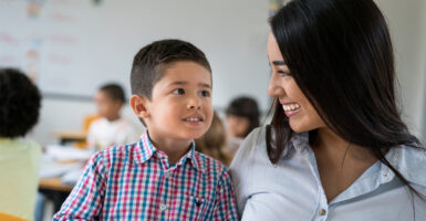 a Latin American teacher with a very young student at school looking very happy