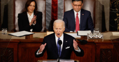 President Joe Biden speaks in to the microphone during the state of the union. Vice President Kamala Harris and House Speaker Mike Johnson are seen seated behind him.