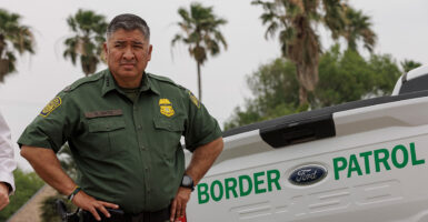 Raul Ortiz stands with his hands on his hips in his Border Patrol uniform with a Border Patrol pickup truck behind him.