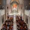 A bird's eye view of the national basilica shows a crowd of parishioners in pews, with large tiled domes above them.