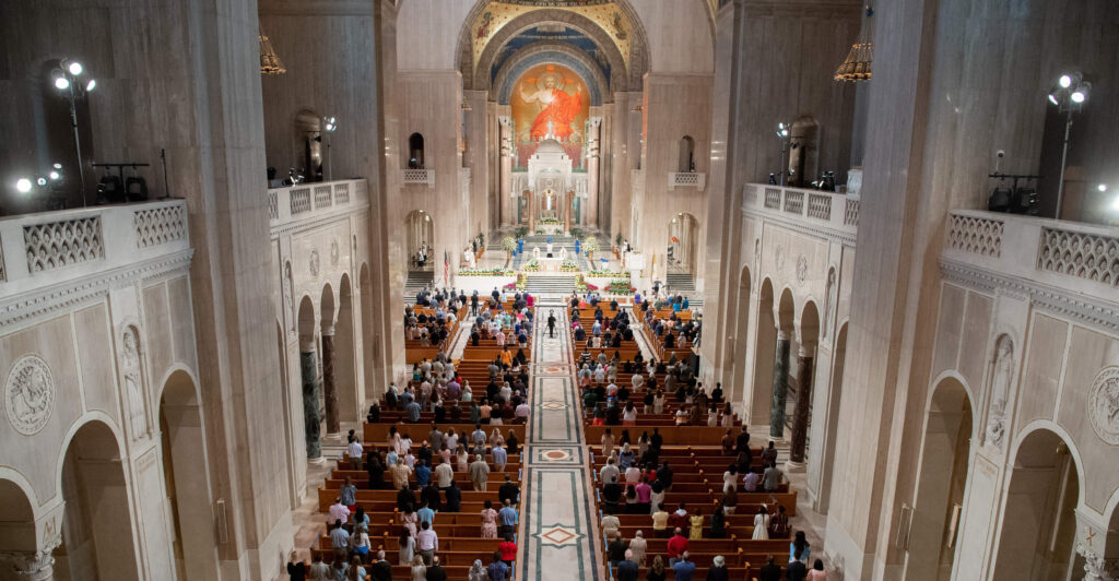 A bird's eye view of the national basilica shows a crowd of parishioners in pews, with large tiled domes above them.