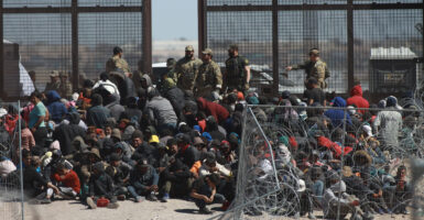Immigrants sit in a large group by the brown border.