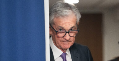 Jerome Powell, an elderly man with grey hair and facial wrinkles, looks down from his glass