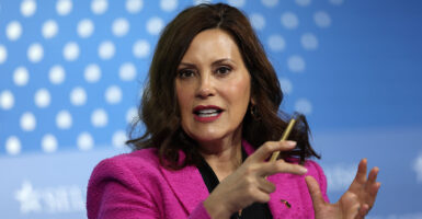 Gretchen Whitmer in a pink blazer gestures with a pencil in her right hand