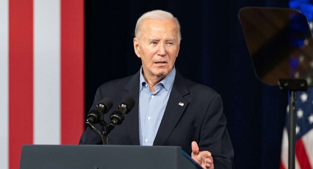 Joe Biden gives a blank look in a black suit with an American flag pin