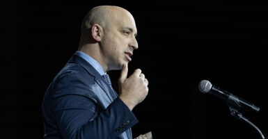 Jonathan Greenblatt in a blue suit gestures in front of a microphone