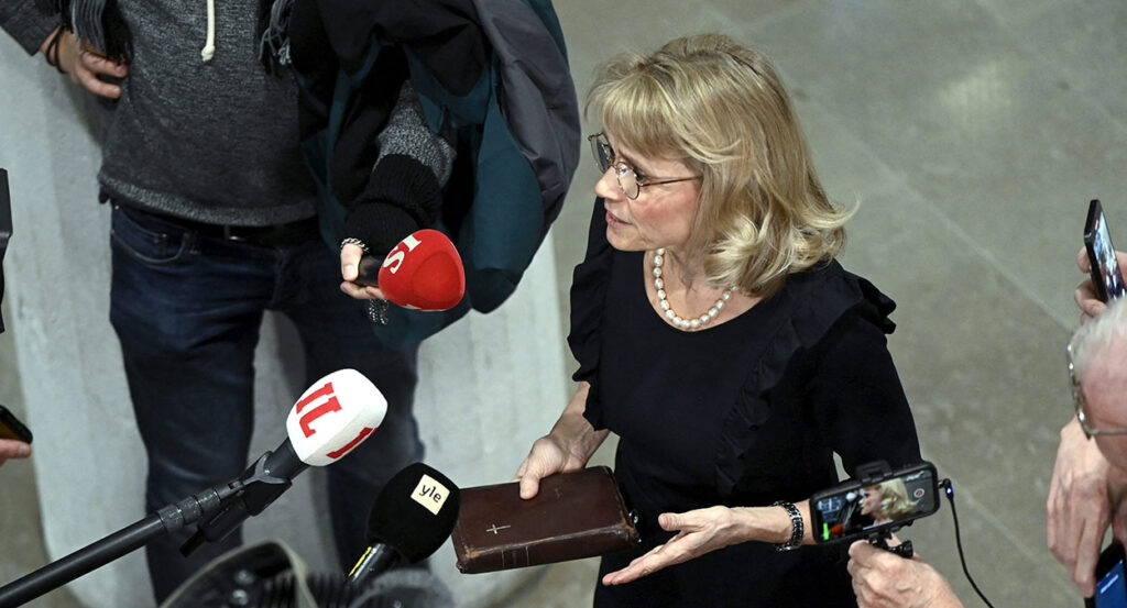 Paivi Rasanen in black holds a Bible accosted by press