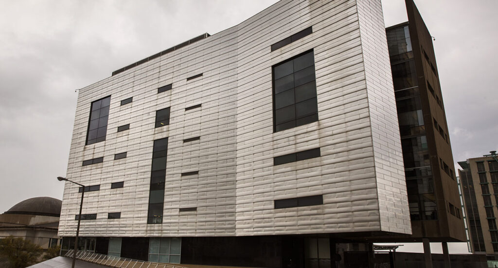 A large grey building with a cloudy rainy sky
